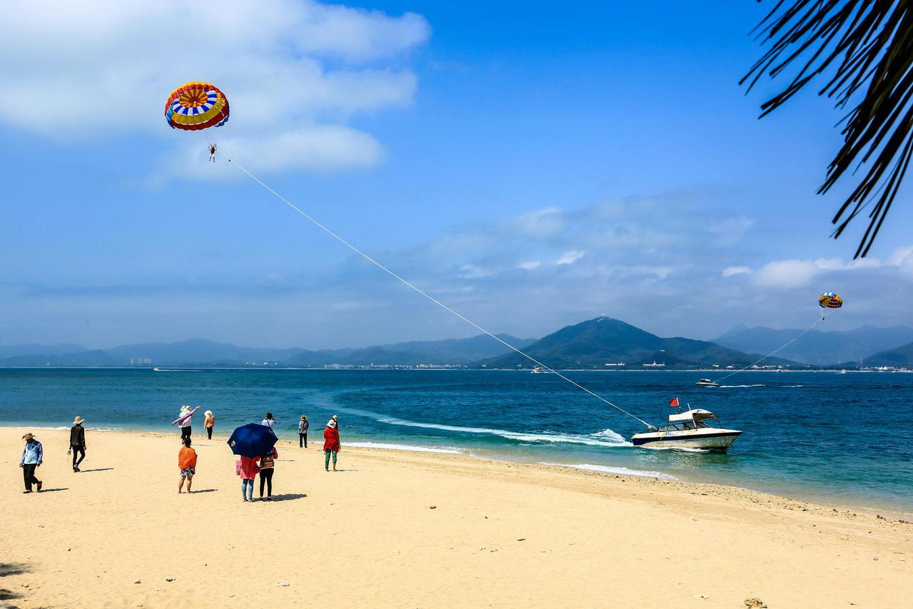 Parasailing experience on Sanya's sandy beach with vibrant sea and mountain backdrop.